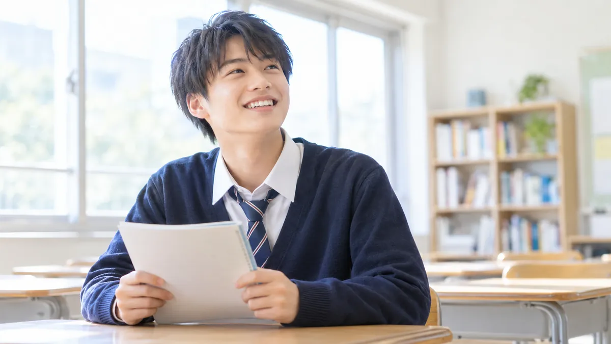 教室でノートを手に、笑顔で前を見る高校生