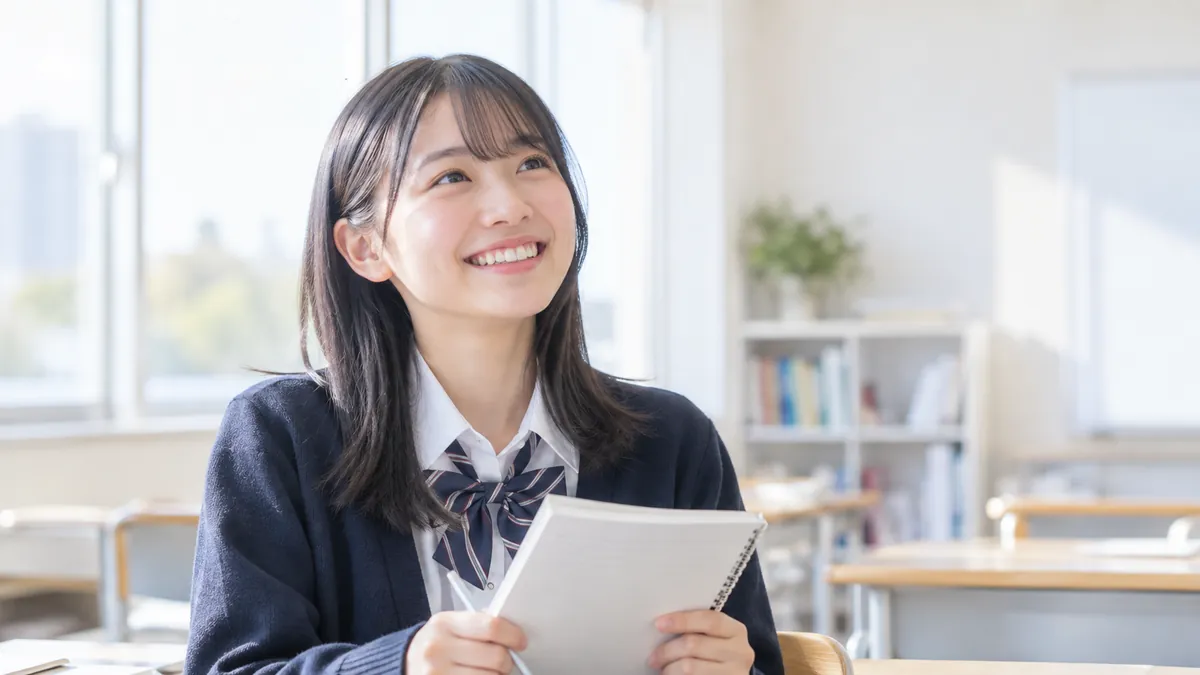 教室でノートを持ち、笑顔で前を見上げる高校生